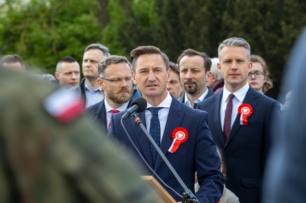 Święto Narodowe Trzeciego Maja - uroczystości przy Pomniku Czynu Polaków. Marszałek Olgierd Geblewicz przemawia do mikrofonu. Obok niego stoją m.in. wojewoda Zbigniew Bogucki i poseł Arkadiusz Marchewka. Za nimi jeszcze kilkanaście osób.