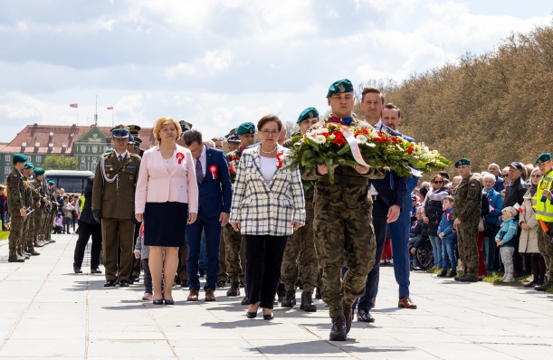 Święto Narodowe Trzeciego Maja - uroczystości w Szczecinie. Marszałek Olgierd Geblewicz i Przewodnicząca Sejmiku Województwa Teresa Kalina składają kwiaty pod Pomnikiem Czynu Polaków. Przed nimi - żołnierz niosący wieniec. Za nimi - inne delegacje.