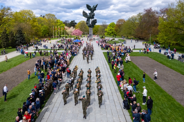 Święto Narodowe Trzeciego Maja - uroczystości przy Pomniku Czynu Polaków. Zdjęcie z drona, na pierwszym planie widać paradującą orkiestrę wojsjową, dalej - kompanię reprezentacyjna. Po bokach - tłum ludzi.