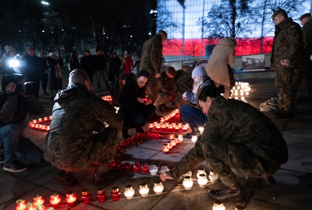 Mieszkańcy odpalają znicze, które jako światełka pamięci utworzą napis GRUDZIEŃ 1970, w tle budynek Filharmonii Szczecińskiej podświetlonej na bialo-czerwono. 
