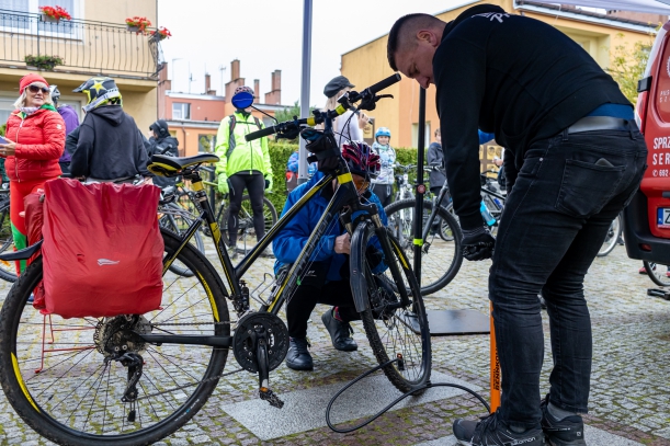 Pompowaniu kół do roweru w mobilnym warsztacie rowerowym, w tle cykliści. 