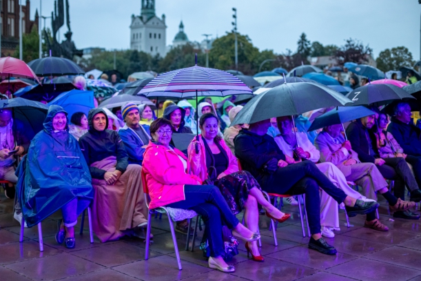 Koncert "Sierpniowe Przełomy" na placu Solidarności w Szczecinie, 27 sierpnia 2023 r. Zdjęcie publiczności siedządzej pod parasolami. Na pierwszym planie - Teresa Kalina, Przewodnicząca Sejmiku Województwa Zachodniopomorskiego. W tle widać wieżę Zamku.