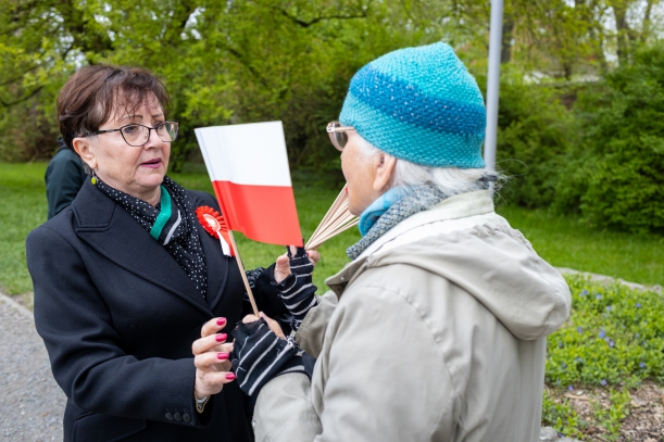 Dzień Flagi Rzeczypospolitej Polskiej. Uroczystości przy Pomniku Czynu Polaków w Szczecinie. Przewodnicząca Sejmiku Województwa Zachodniopomorskiego Teresa Kalina przekazuje starszej kobiecie biało-czerewoną chorągiewkę.