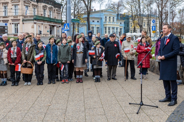 Uroczystość z okazji Narodowego Święta Niepodległości przy pomniku marszałka Józefa Piłsudskiego w Szczecinie. Przy mikrofonie marszałek województwa Olgierd Geblewicz. Obok - kilkadziesiat osób, w tym grupa harcerzy, z biało-czerwonymi chorągiewkami.