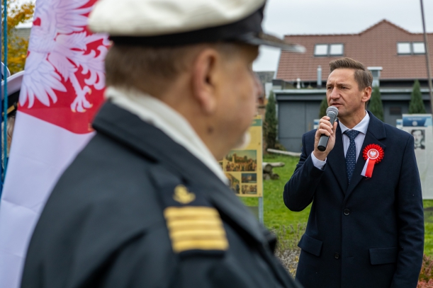 Marszałek województwa Olgierd Geblewicz przemawia podczas uroczystości z okazji Narodowego Święta Niepodległości. W klapę granatowego płaszcza ma wpięty biało-czerwony kotylion. Na pierwszym planie widać polską banderę i oficera w marynarskim mundurze.