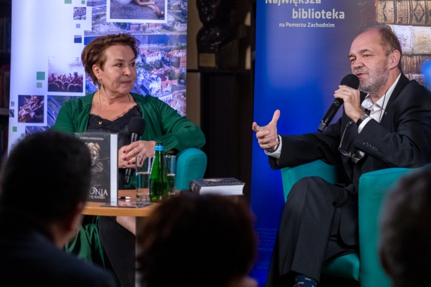 Spotkanie "Sydonia i Gryfici" (z cyklu "Otwarta społeczność") w Książnicy Pomorskiej. Na scenie - pisarka Elżbieta Cherezińska i prowadzący debatę o. Tomasz Dostatni (trzyma mikrofon, mówi i gestykuluje).