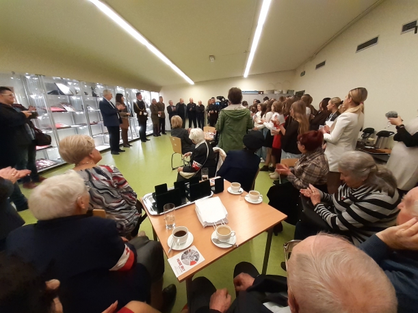 Wernisaż wystawy "Polskie orły" w Centrum Dialogu Przełomy w Szczecinie (27 października 2022 r.). Kilkadziesiąt osób zgromadzonych w sali, w której przy ścianie ustawione są oświetlone gabloty. Na pierwszym planie widać kilku siedzących kombatantów.  