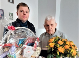 Zastępca dyrektora Gabinetu Marszałka Marcin Kordela z wizytą u 102-letniego Leona Wałowskiego (w dniu urodzin, 4 kwietnia). Pan Leon pozuje do zdjęcia, trzymając bukiet kwiatów. M.Kordela trzyma kosz ze słodkościami i wielkanocnymi ozdobami.