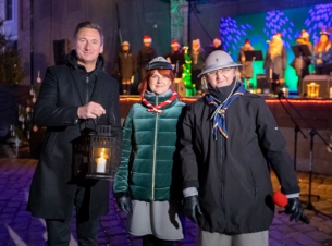 Marszałek Olgierd Geblewicz na dużym dziedzińcu Zamku Książąt Pomorskich pozuje do zdjęcia z Betlejemskim Światłem Pokoju. Obok stoją dwie kobiety w harcerskich czapkach, pod kurtkami widać mundury.