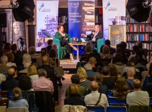 Spotkanie "Sydonia i Gryfici" (z cyklu "Otwarta społeczność") w Książnicy Pomorskiej. Na scenie - pisarka Elżbieta Cherezińska i prowadzący debatę o. Tomasz Dostatni. Na pierwszym planie - publiczność. Kilkadziesiąt osób siedzi na krzesłach.